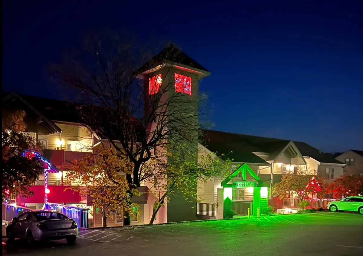 A cheerful exterior view featuring decorative lighting on the building, with a prominent clock tower and a green entrance sign, suggesting festivities and a welcoming community environment.