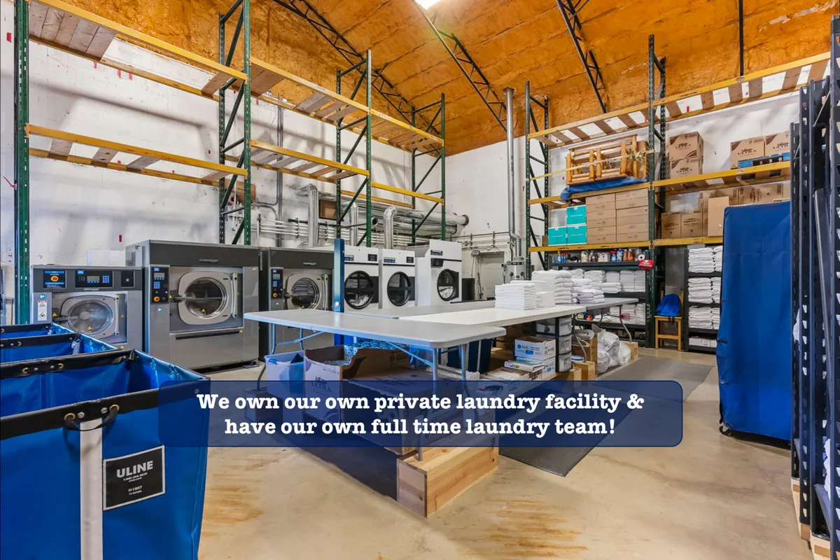 This image displays a modern, well-equipped laundry room with industrial laundry machines, a spacious folding table, storage shelves, and laundry bins. The setup conveys efficiency and the convenience of in-unit laundry amenities.