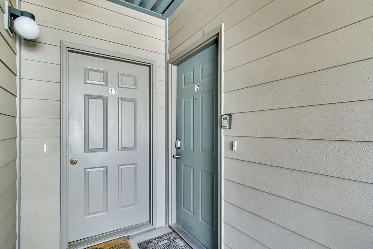 A welcoming building common area showing two doors (11 and 12) with a cheerful welcome mat outside. The entryway hints at easy arrivals and a sense of belonging for guests.