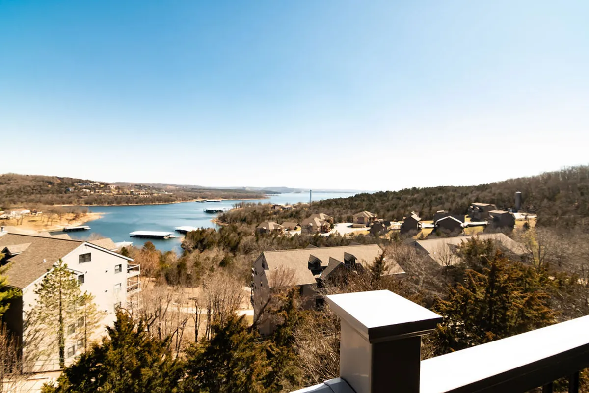 A tranquil view from the condo balcony shows the sparkling Table Rock Lake framed by trees and surrounded by lakeside homes. The water stretches out invitingly, with boats gliding across its surface and the peaceful shoreline in full view, perfectly capturing the lake's beauty and recreational spirit.