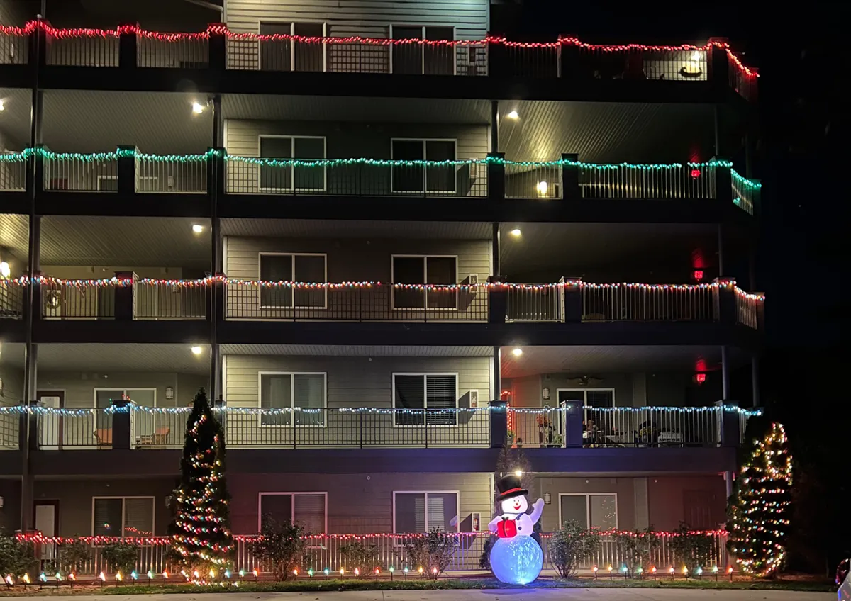 This cheerful exterior shot features the building adorned with decorative lights, a snowman decoration in the foreground, and a Christmas tree nearby. The scene suggests a joyful, community-oriented environment, ideal for memorable group photos and holiday gatherings.