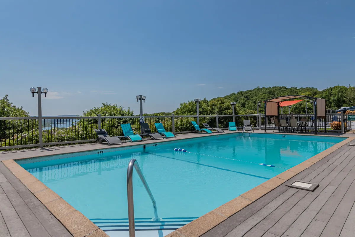 A sunlit resort-style outdoor pool surrounded by lounge chairs and landscaped greenery, with an inviting seating area nearby. The scene exudes relaxation and leisure, perfect for socializing or unwinding after a day on the lake.